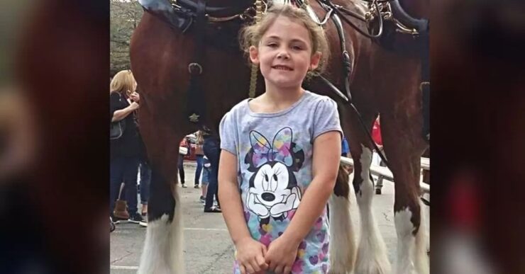 Bambina posa felice davanti a un cavallo